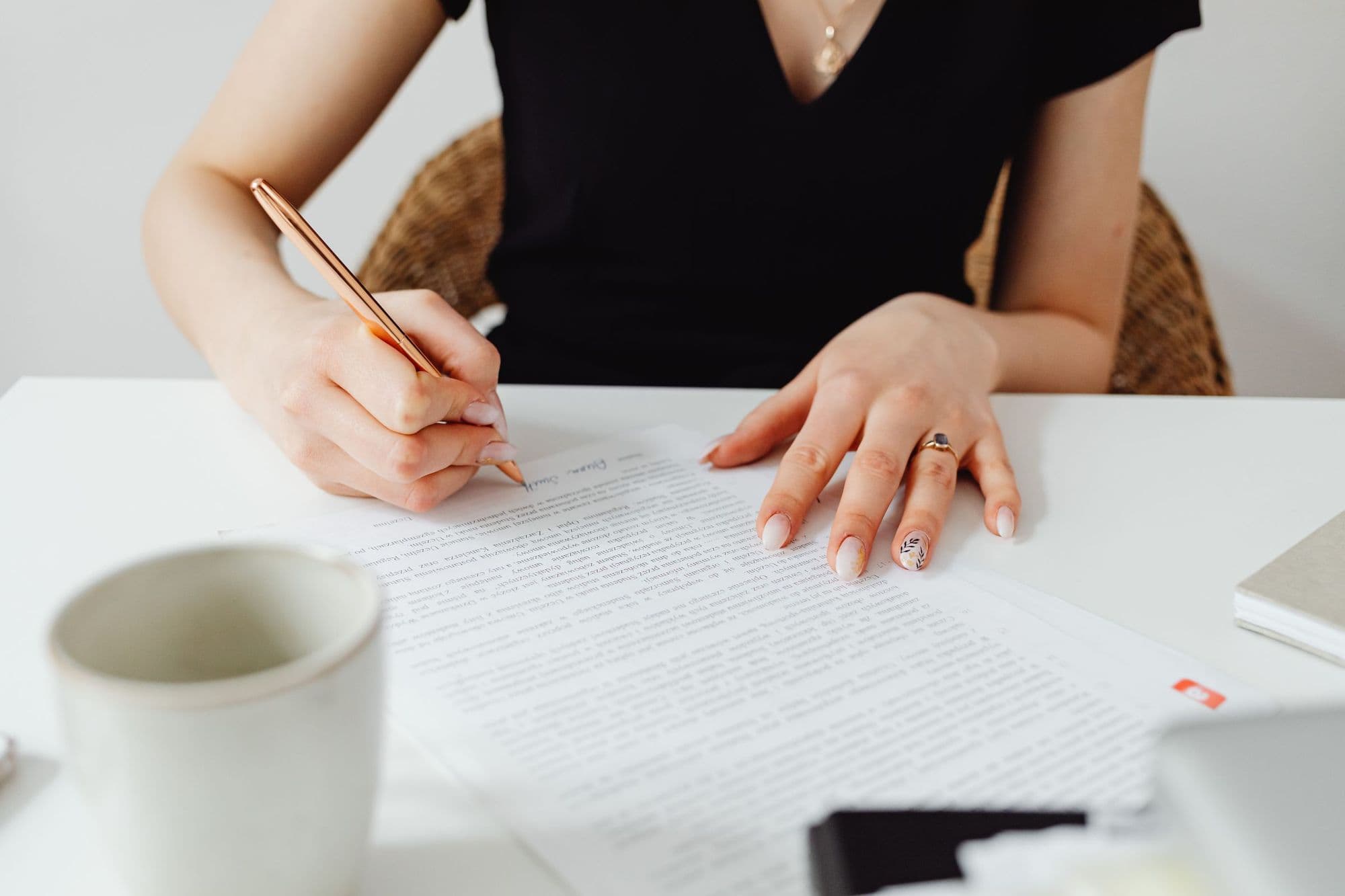 A woman's hands signing a document with a pen, in black and white